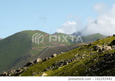 Winding mountain road across green hills under clear sky Winding mountain road across green hills under clear sky 142243442