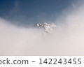 Snow covered mountain peaks emerging through thick white clouds 142243455