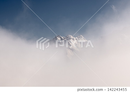 Snow covered mountain peaks emerging through thick white clouds Snow covered mountain peaks emerging through thick white clouds 142243455