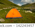 Bright orange camping tent in a grassy mountain valley 142243457