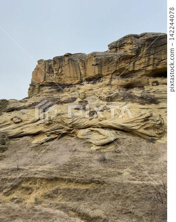 Eroded sandstone rock with layered formations and dry soil foreground. Eroded sandstone rock with layered formations and dry soil foreground. 142244078