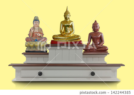 front view features three distinct sacred statues displayed on a tiered, white wood altar stand against a solid pale yellow background, religion, buddha, copy space front view features three distinct sacred statues displayed on a tiered, white wood altar stand against a solid pale yellow background, religion, buddha, copy space 142244385