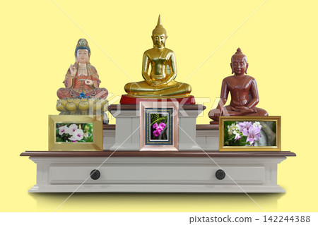 front view traditional multi-tiered wooden altar table featuring three religious statues and three framed floral pictures on yellow background, copy space front view traditional multi-tiered wooden altar table featuring three religious statues and three framed floral pictures on yellow background, copy space 142244388