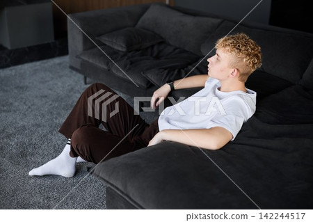Young man reclining on couch, casual reflective moment Young man reclining on couch, casual reflective moment 142244517