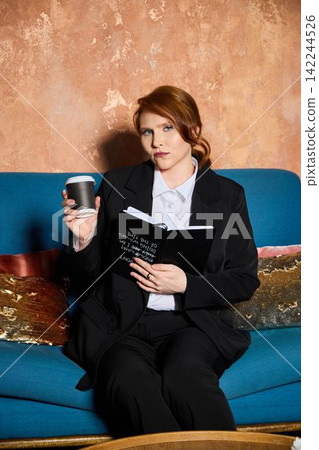 Professional individual reviews documents while sipping coffee comfortably Professional individual reviews documents while sipping coffee comfortably 142244526