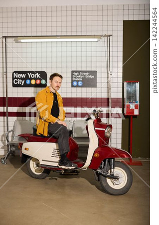 Man sitting casually on vintage scooter at busy New York subway station 142244564