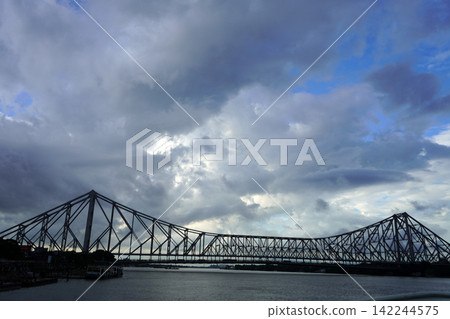Howrah Bridge silhouette against a dramatic cloudy sky over the Hooghly River in Kolkata Howrah Bridge silhouette against a dramatic cloudy sky over the Hooghly River in Kolkata 142244575