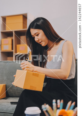 Startup SME small business entrepreneur of freelance Asian woman wearing apron using laptop and box to receive and review orders online to prepare to pack sell to customers, online sme business ideas. Startup SME small business entrepreneur of freelance Asian woman wearing apron using laptop and box to receive and review orders online to prepare to pack sell to customers, online sme business ideas. 142244657