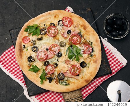 Baked pizza with chicken, tomatoes and olives on a black table Baked pizza with chicken, tomatoes and olives on a black table 142244929