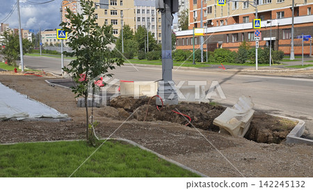 A young tree grows beside a trench near a sidewalk repair site on a residential city street during daylight. A young tree grows beside a trench near a sidewalk repair site on a residential city street during daylight. 142245132
