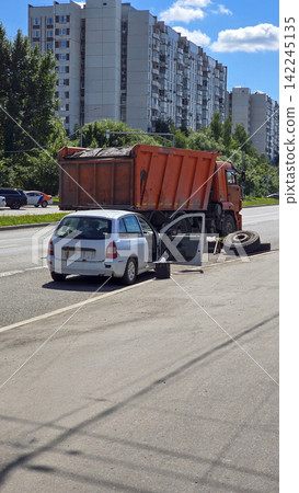 A white car and an orange dump truck parked on a city street near apartment buildings on a summer day time. A white car and an orange dump truck parked on a city street near apartment buildings on a summer day time. 142245135