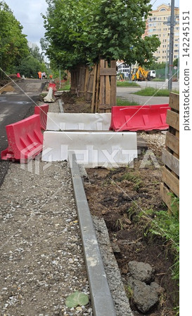 Red and white plastic barriers cordon off a sidewalk reconstruction site near trees in a residential area. 142245151