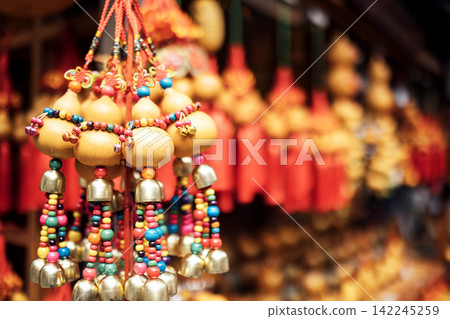 Colorful decorative hanging ornaments with beads and bells displayed in a market, showcasing traditional craftsmanship and vibrant colors in a festive setting Colorful decorative hanging ornaments with beads and bells displayed in a market, showcasing traditional craftsmanship and vibrant colors in a festive setting 142245259