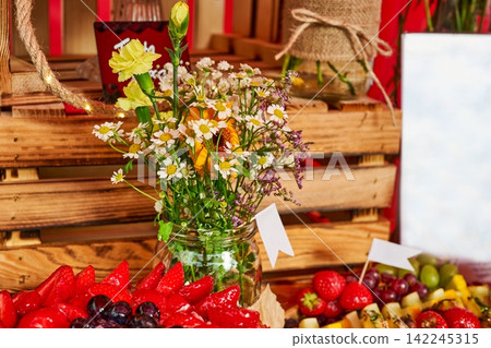 Rustic wooden crate display with a glass jar of fresh wildflowers and chamomile alongside ripe red strawberries Rustic wooden crate display with a glass jar of fresh wildflowers and chamomile alongside ripe red strawberries 142245315