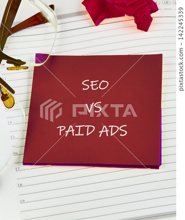 Digital marketing strategy concept showing SEO vs Paid Ads written on a red square paper placed over an open daily planner 142245339