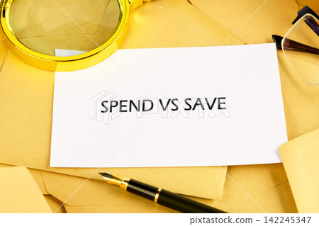 Personal finance concept showing Spend vs Save written on a white card resting on a pile of brown envelopes with a pen Personal finance concept showing Spend vs Save written on a white card resting on a pile of brown envelopes with a pen 142245347