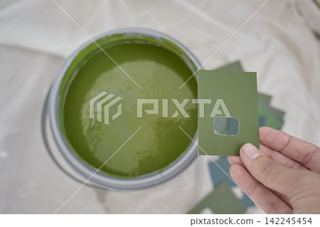 Hand holds green paint sample beside open can of similar green paint Hand holds green paint sample beside open can of similar green paint 142245454