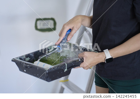 Person loads roller with green paint in tray before painting interior wall Person loads roller with green paint in tray before painting interior wall 142245455