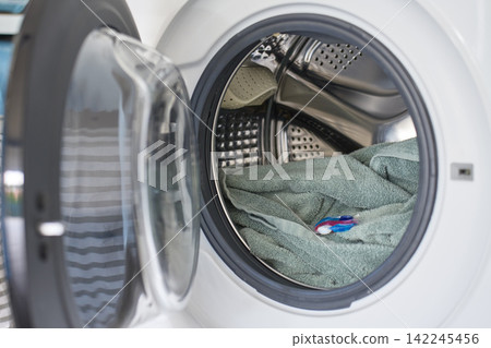 Open washing machine with towel and detergent capsule inside drum Open washing machine with towel and detergent capsule inside drum 142245456