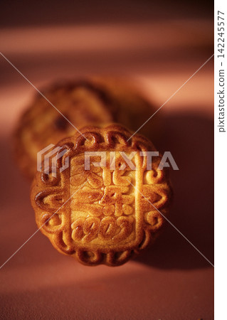 Mooncake with intricate design featuring Chinese characters, placed on a soft pink surface, symbolizing the Mid-Autumn Festival celebration and cultural traditions Mooncake with intricate design featuring Chinese characters, placed on a soft pink surface, symbolizing the Mid-Autumn Festival celebration and cultural traditions 142245577
