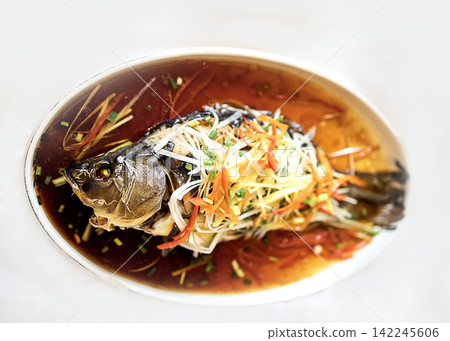 Whole fish dish garnished with julienned vegetables served in a white oval plate with a rich brown sauce on a light background Whole fish dish garnished with julienned vegetables served in a white oval plate with a rich brown sauce on a light background 142245606