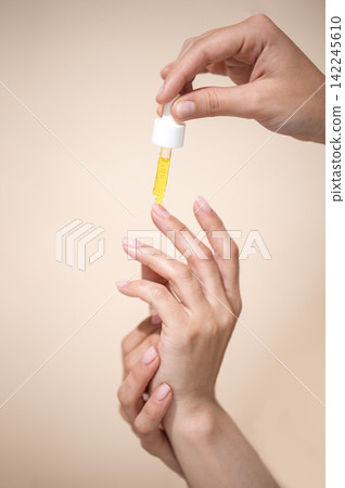 Hands applying yellow serum from dropper onto fingers against a soft beige background, showcasing skincare routine and beauty treatment Hands applying yellow serum from dropper onto fingers against a soft beige background, showcasing skincare routine and beauty treatment 142245610