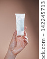 Hand holding a transparent tube of gel with bubbles against a soft brown background, showcasing a cosmetic or skincare product for personal care use 142245713