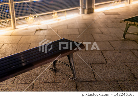 An empty outdoor bench illuminated by warm lighting. An empty outdoor bench illuminated by warm lighting. 142246163