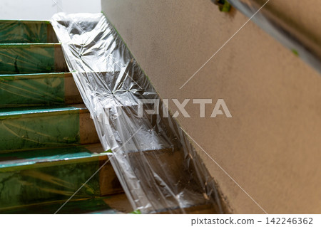 Staircase of a building covered in protective sheeting in preparation for painting work. Staircase of a building covered in protective sheeting in preparation for painting work. 142246362