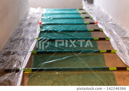 Stairs covered with green protective sheeting and masking tape Stairs covered with green protective sheeting and masking tape 142246366