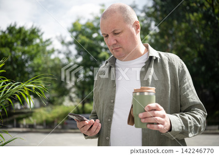Mature freelancer with smartphone and reusable coffee cup outdoors Mature freelancer with smartphone and reusable coffee cup outdoors 142246770