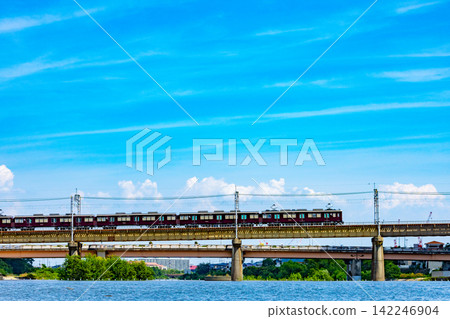 A Hankyu train crossing the Mukogawa River against a summer blue sky: A railway scene in Takarazuka City, Hyogo Prefecture. 142246904