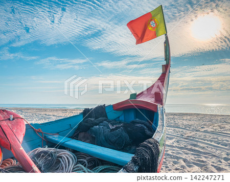 Traditional Portuguese fishing boat with national flag on sunny sandy beach Traditional Portuguese fishing boat with national flag on sunny sandy beach 142247271