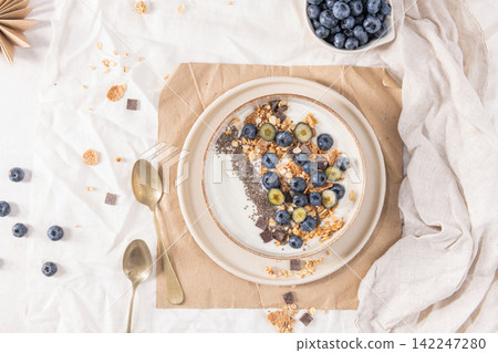 Healthy breakfast bowl with yogurt granola blueberries and chia seeds served in a rustic dish for a nutritious start to the day on white fabric Healthy breakfast bowl with yogurt granola blueberries and chia seeds served in a rustic dish for a nutritious start to the day on white fabric 142247280