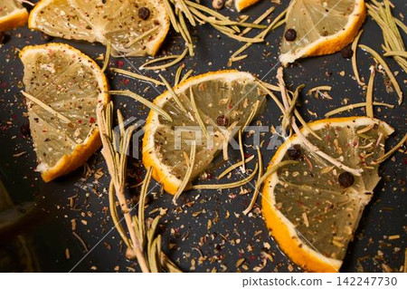 Orange slices roast with rosemary herbs peppers and sea salt on dark baking sheet closeup showing bright citrus zest and glossy oil, with orange, slice, citrus, rosemary detail Orange slices roast with rosemary herbs peppers and sea salt on dark baking sheet closeup showing bright citrus zest and glossy oil, with orange, slice, citrus, rosemary detail 142247730