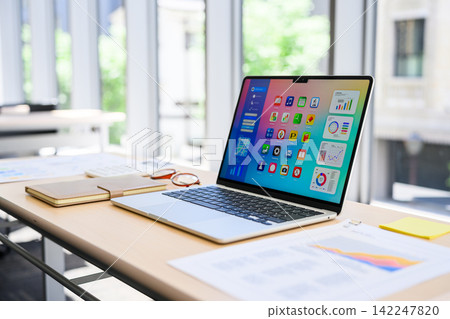 A desk with a laptop open with business applications and graphs. A desk with a laptop open with business applications and graphs. 142247820