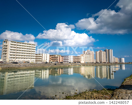 A beautiful urban landscape in Higashihama, Yonabaru Town, Okinawa Prefecture, with apartment buildings reflected in the water, against a blue sky and clouds. A beautiful urban landscape in Higashihama, Yonabaru Town, Okinawa Prefecture, with apartment buildings reflected in the water, against a blue sky and clouds. 142248057