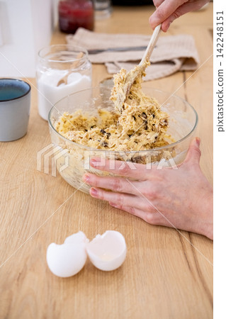 Bakery process. Mixing dough. Female chef hand stirring sweet mass with raisins oat flakes for healthy confectionery treat production. Bakery process. Mixing dough. Female chef hand stirring sweet mass with raisins oat flakes for healthy confectionery treat production. 142248151