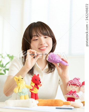 A young woman enjoying making stuffed animals at a table. A young woman enjoying making stuffed animals at a table. 142249872