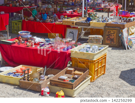 Antique market stalls: A variety of antique goods and tableware displayed on a table with a red tablecloth and in yellow containers. Antique market stalls: A variety of antique goods and tableware displayed on a table with a red tablecloth and in yellow containers. 142250299