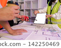 Engineers holding digital tablet mockup and walkie talkie over blueprint for construction planning 142250469