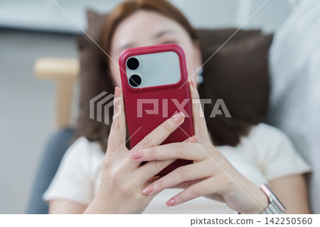 Close up of woman holding red smartphone while relaxing at home Close up of woman holding red smartphone while relaxing at home 142250560