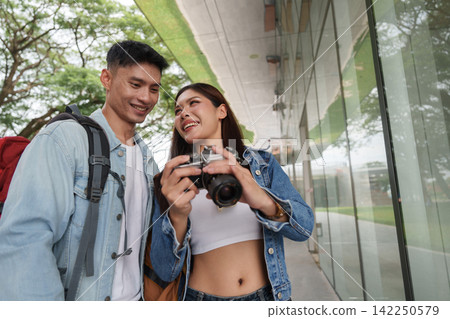 Asian couple traveling together taking photos with camera on city street for vacation getaway Asian couple traveling together taking photos with camera on city street for vacation getaway 142250579