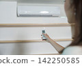 Cropped hand holding remote control to adjust air conditioner temperature at home 142250585