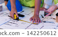 Cropped hands measuring blueprint with tape measure for architectural design and construction planning 142250612