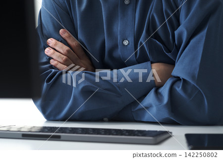 A businessman sits in front of his office computer with his arms crossed, contemplating a problem. (Image caption: Man and desktop computer) A businessman sits in front of his office computer with his arms crossed, contemplating a problem. (Image caption: Man and desktop computer) 142250802