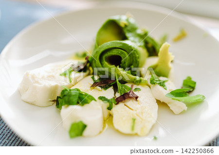 Healthy caprese salad variation with fresh avocado slices and mozzarella cheese Healthy caprese salad variation with fresh avocado slices and mozzarella cheese 142250866