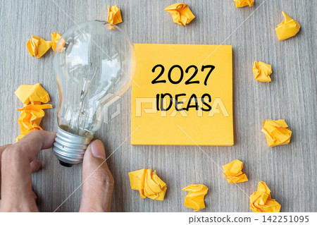 2027 Idea words on yellow note and crumbled paper with Businessman holding lightbulb on wooden table background. New Year New Start Creative, Innovation, Imagination, Resolution and Goal concept 2027 Idea words on yellow note and crumbled paper with Businessman holding lightbulb on wooden table background. New Year New Start Creative, Innovation, Imagination, Resolution and Goal concept 142251095