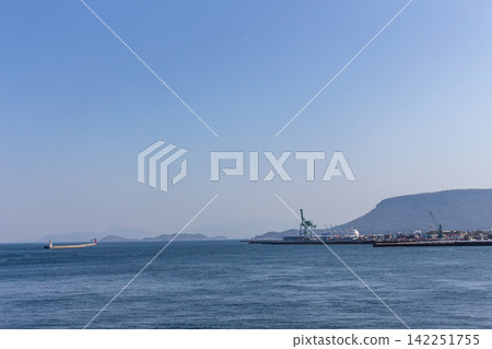 A harbor landscape with a clear blue sky and calm sea, container cranes, and a breakwater. A harbor landscape with a clear blue sky and calm sea, container cranes, and a breakwater. 142251755