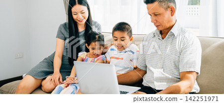 A cheerful family seated on a cozy sofa sharing a laptop parents and kids engaged in online browsing A cheerful family seated on a cozy sofa sharing a laptop parents and kids engaged in online browsing 142251971